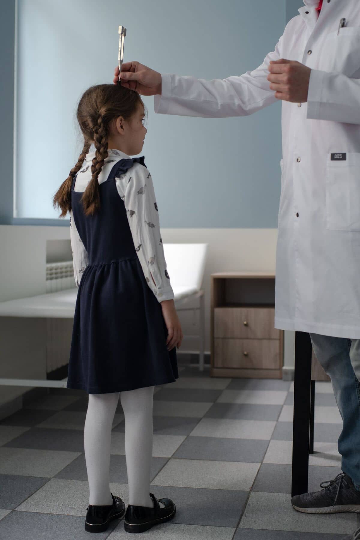 Девочка с косичками и в тёмно-синем платье стоит неподвижно