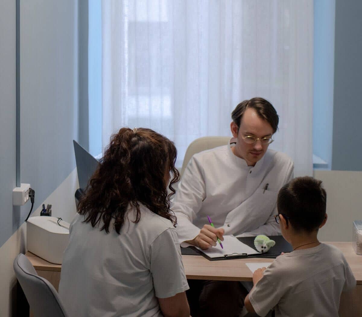 Врач в белом халате сидит за столом в тихом, мягко освещённом кабинете