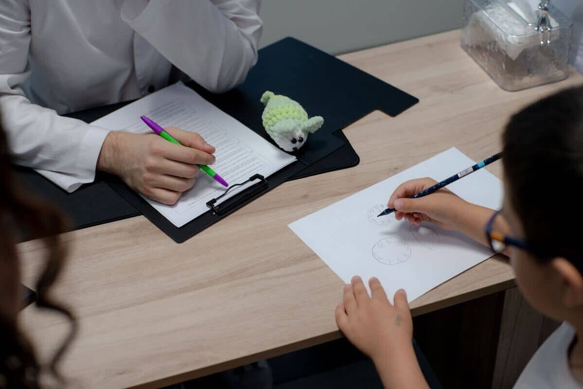 Ребёнок выполняет задание по рисованию часов во время консультации с врачом.