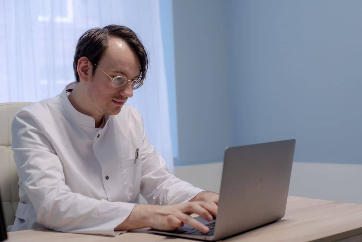 Человек в белом халате работает за ноутбуком в светлом офисе