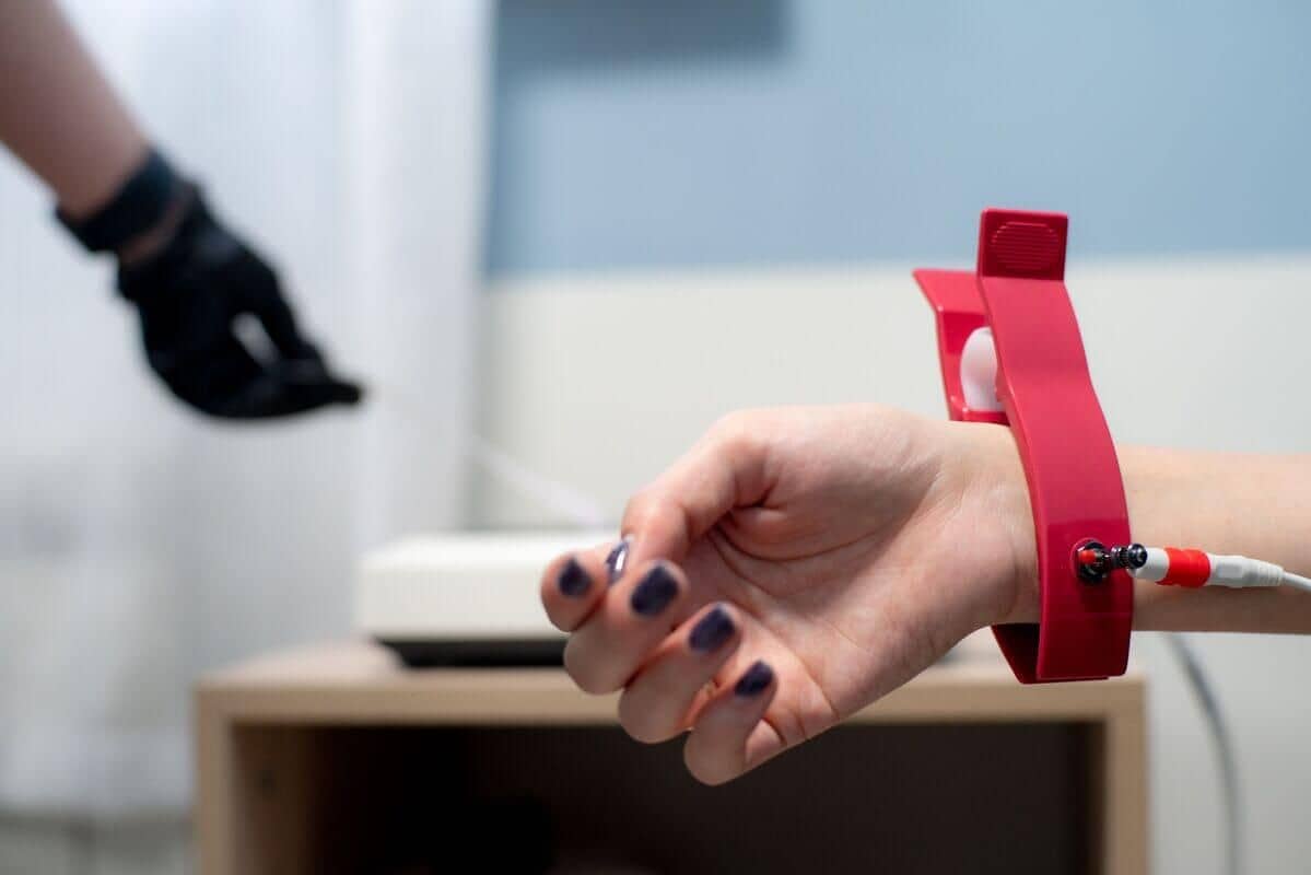 На столе лежит рука с накрашенными ногтями и красным браслетом