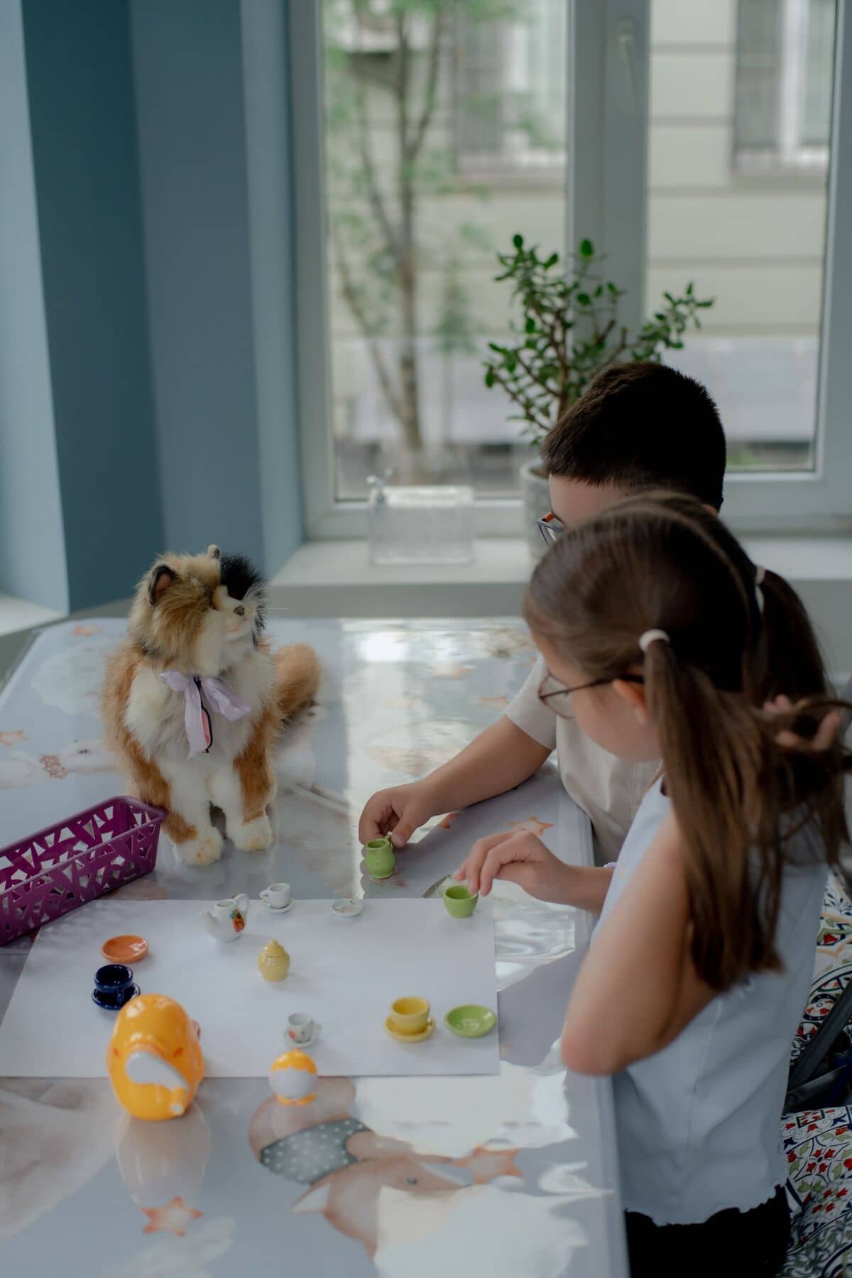 Двое детей играют с игрушечным чайным сервизом на столе