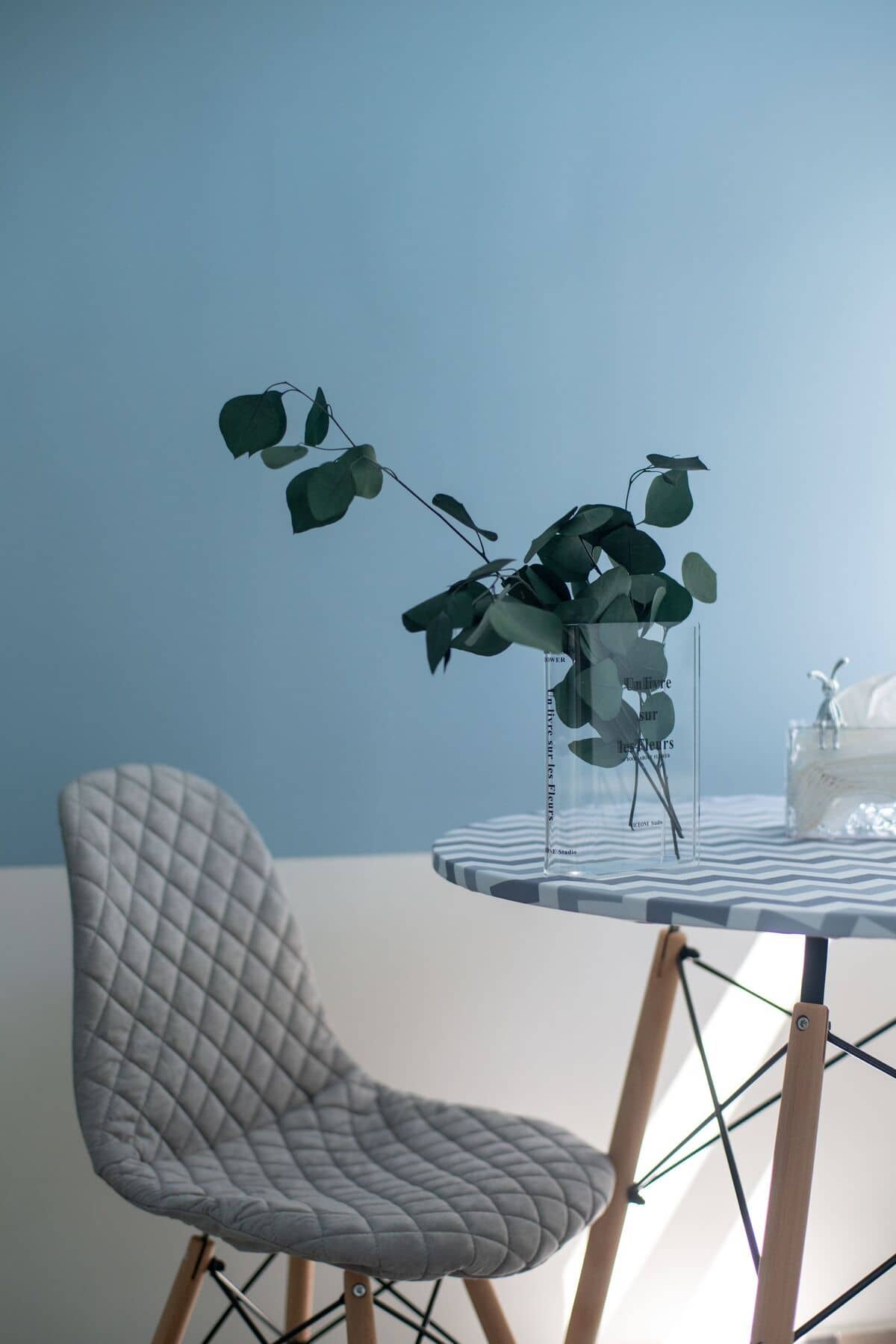 Современный интерьер со светло-голубой стеной, серым стёганым стулом и круглым столом