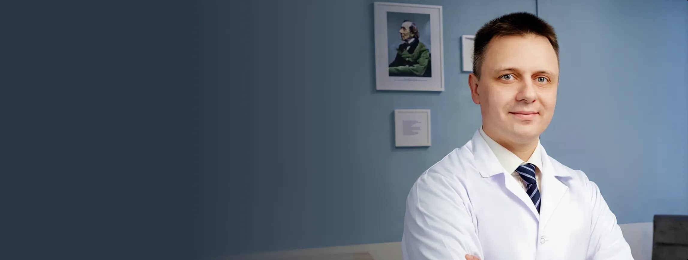 Уверенный в себе врач-мужчина в белом халате и галстуке улыбается, стоя на фоне синей стены