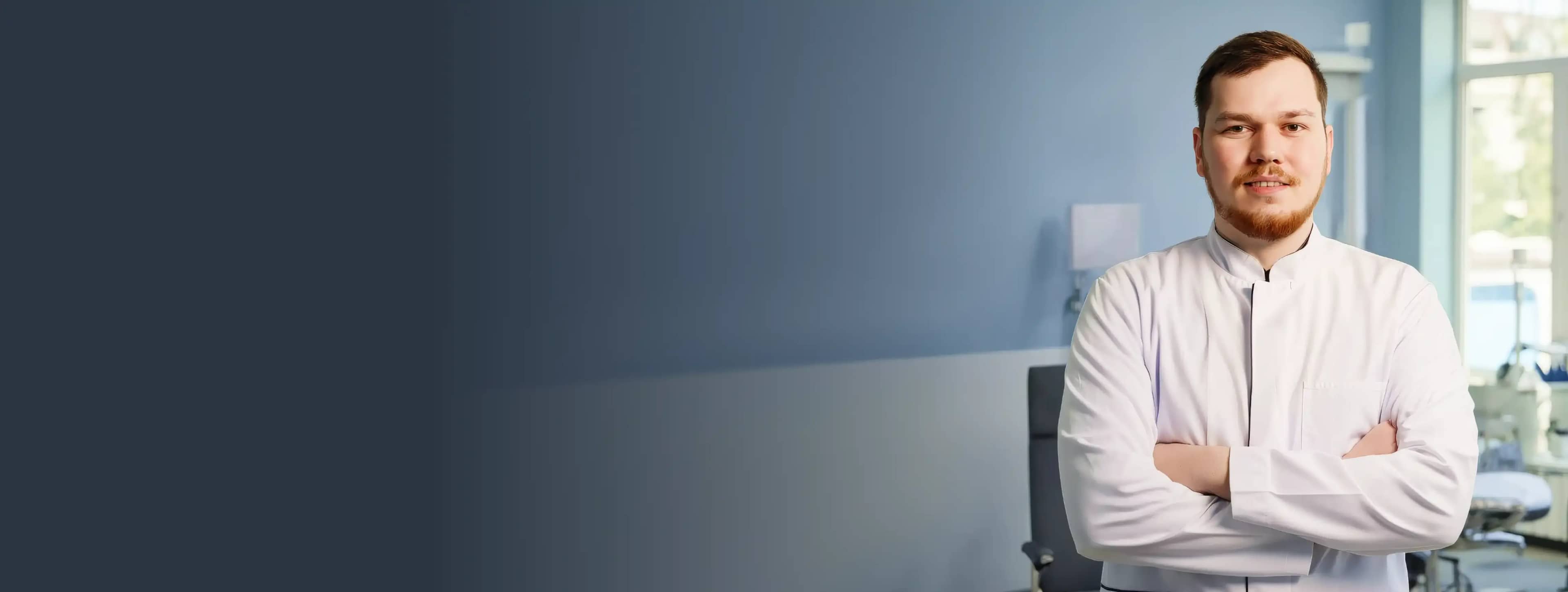 Уверенный в себе мужчина в белом халате стоит, скрестив руки, в современном медицинском кабинете