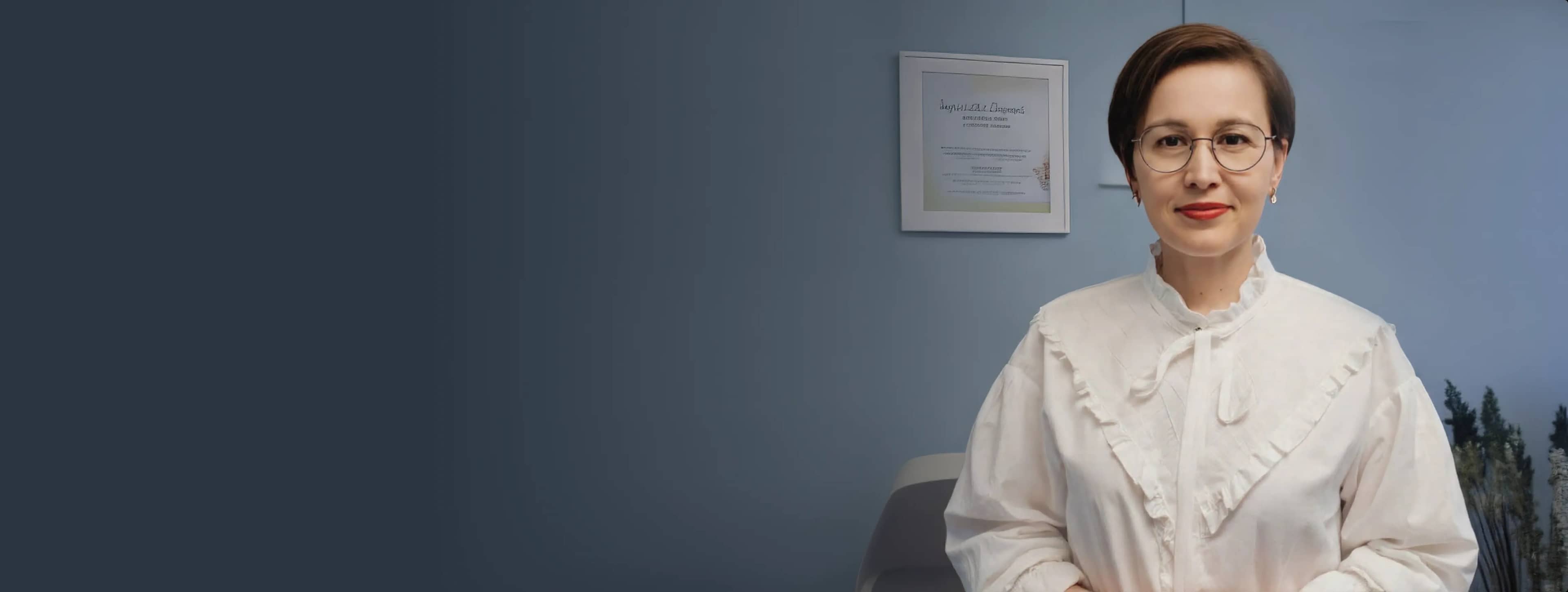 Женщина в белой блузке с рюшами стоит в офисе с синими стенами