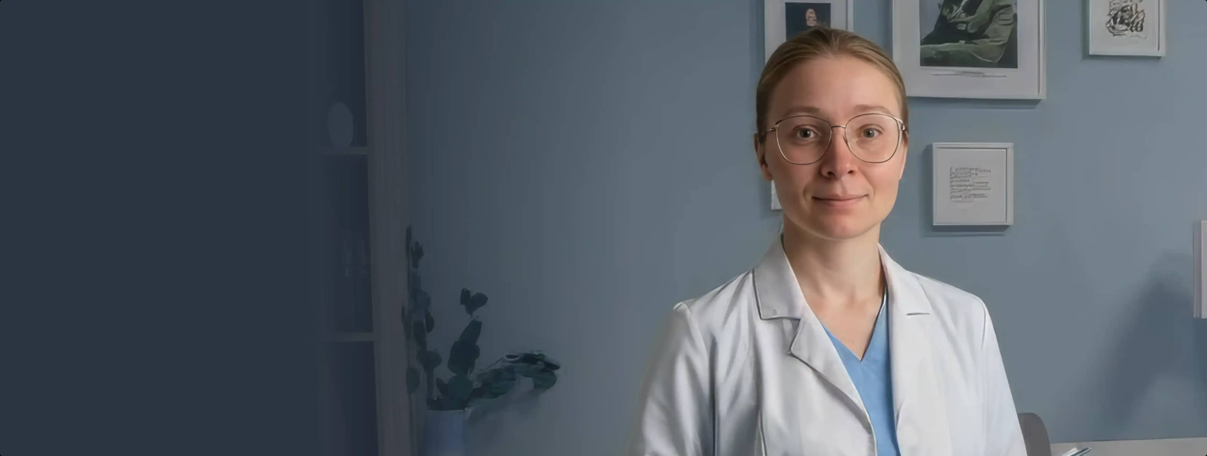 Женщина в очках и белом халате стоит в мягко освещенной комнате с синими стенами