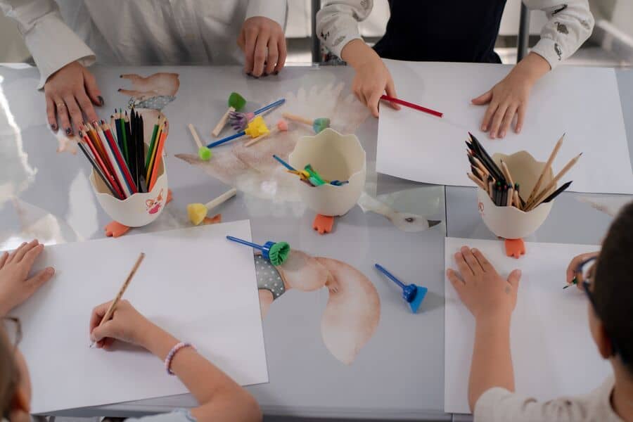 Дети рисуют за столом белой бумагой и цветными карандашами
