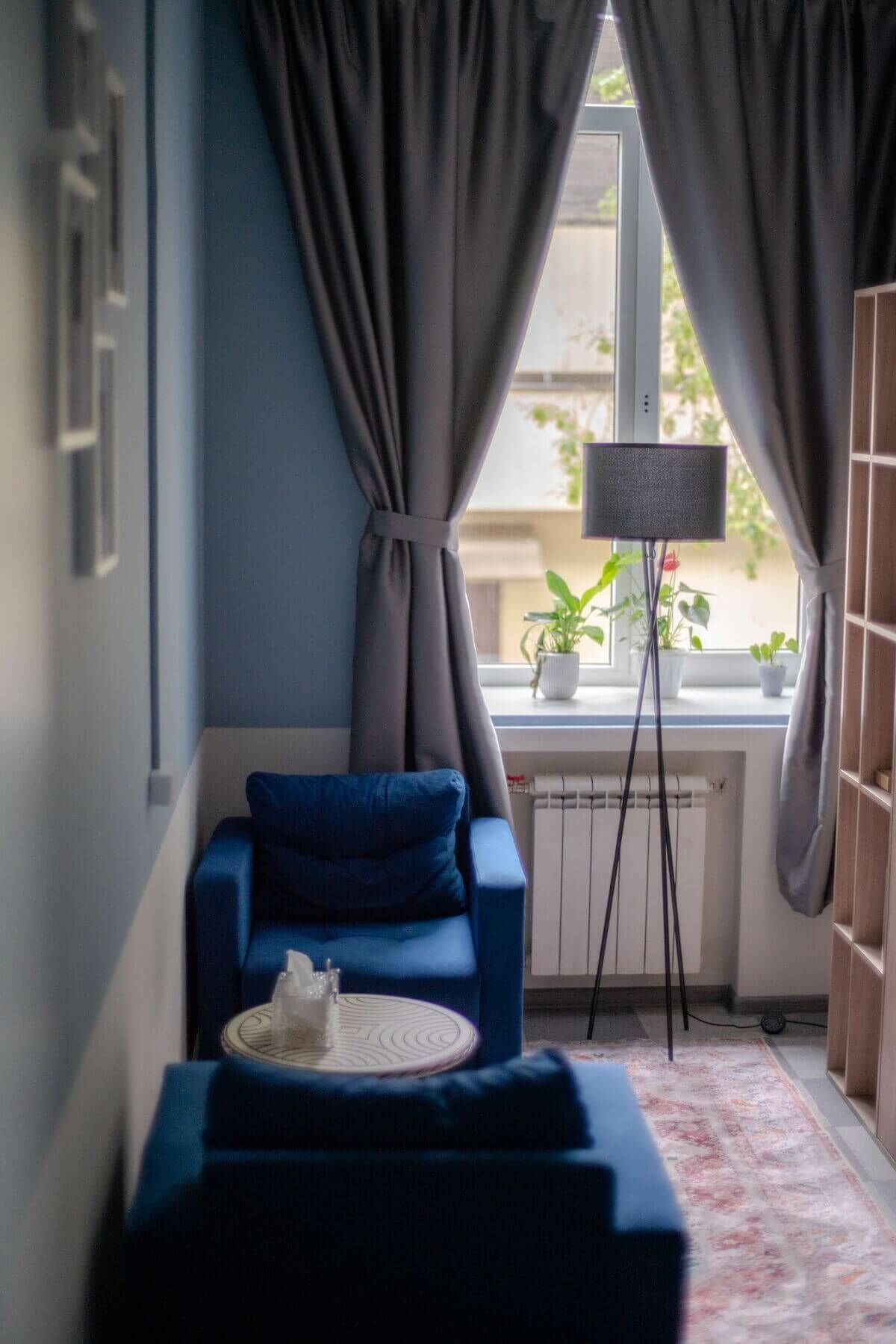 Уютная комната с синими креслами, круглым столом, коробкой салфеток и узорчатым ковром