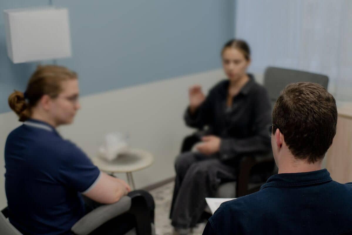 В светло-голубой комнате сидят три человека на консультации