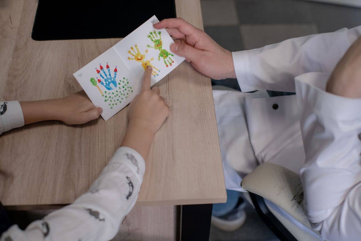 Ребенок указывает на красочный отпечаток руки, который держит взрослый в белом халате