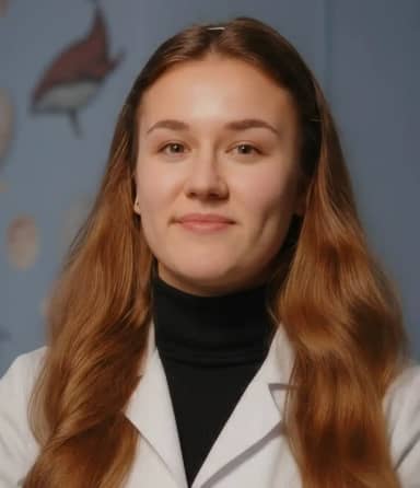 Женщина с длинными каштановыми волосами, в белом лабораторном халате и чёрной водолазке